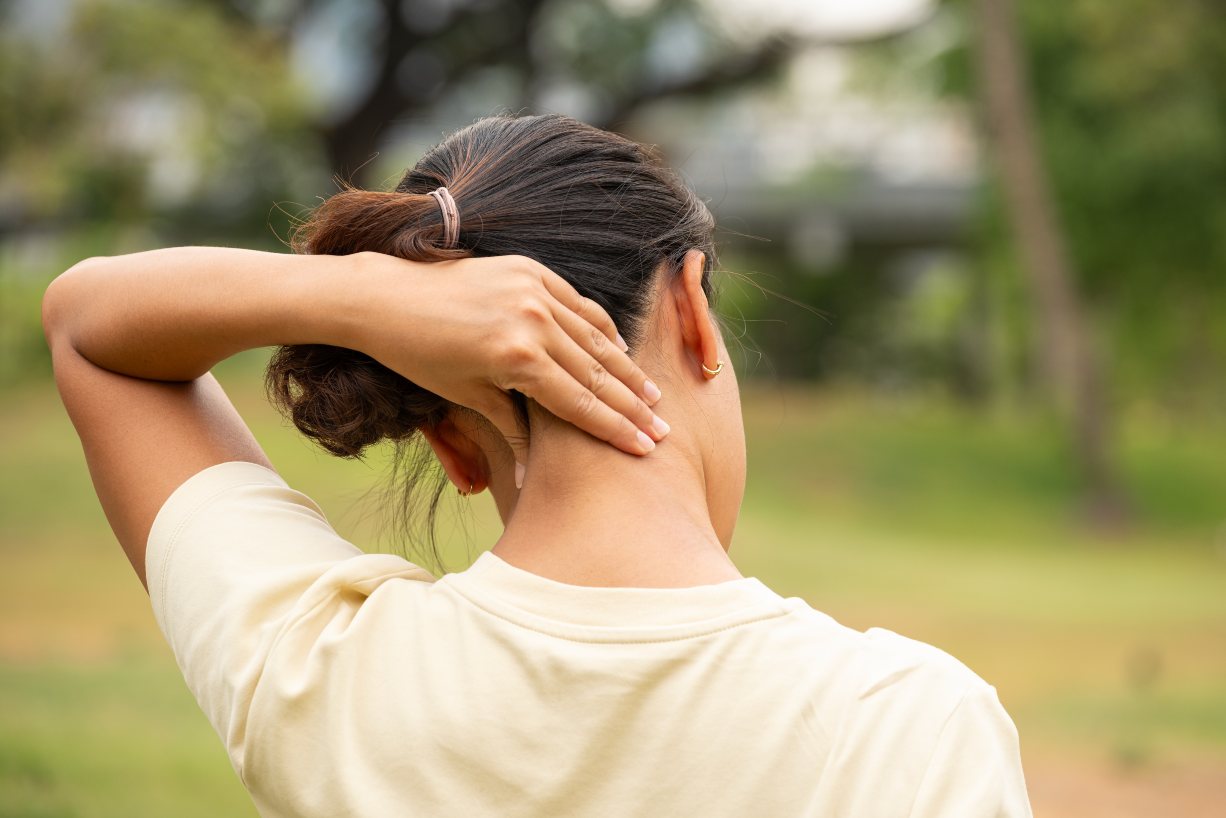 Woman in Pearland, TX, squeezing her neck to relieve a stiff neck in a grassy area