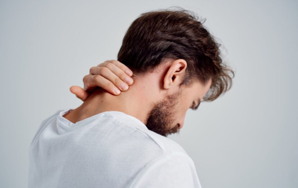 A man in a white shirt, holding the back of his neck, is experiencing neck pain in Pearland, TX
